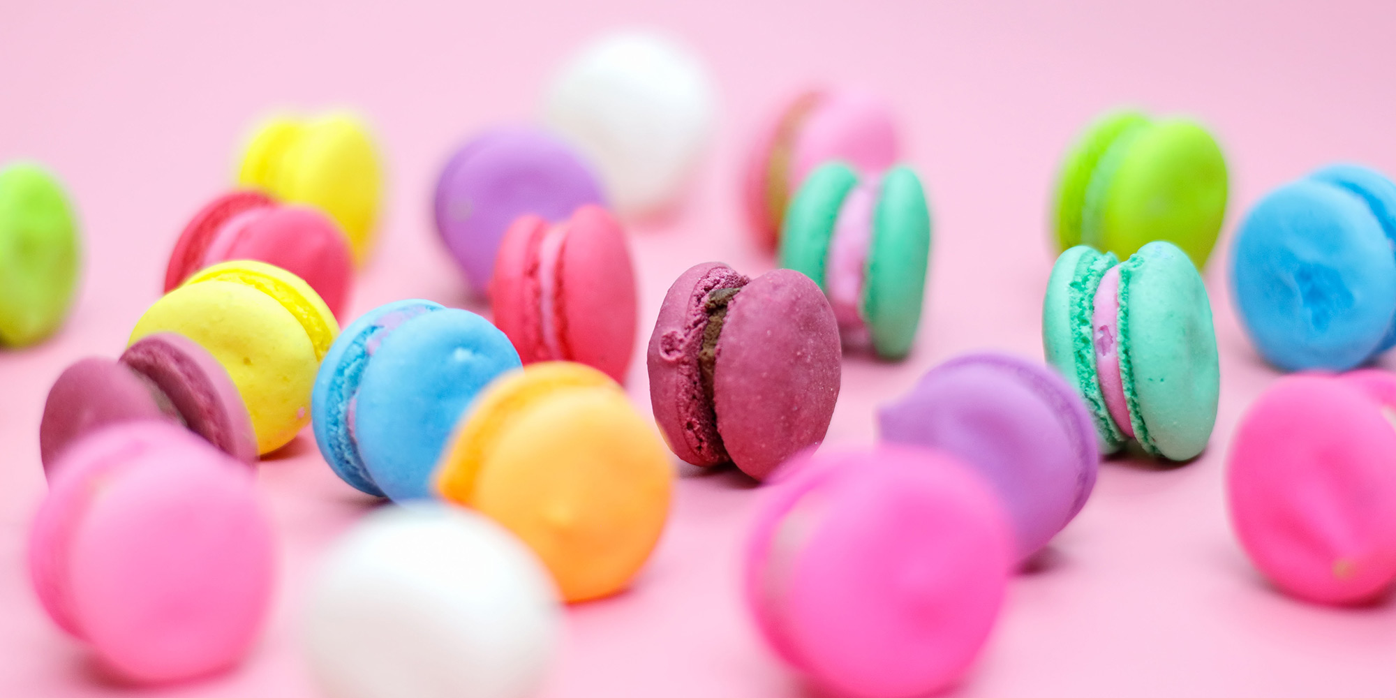 pink, blue, green, yellow, and purple macaron cookies against pink background