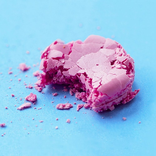 bright pink macaron cookie half-eaten with crumbs beside it against blue background
