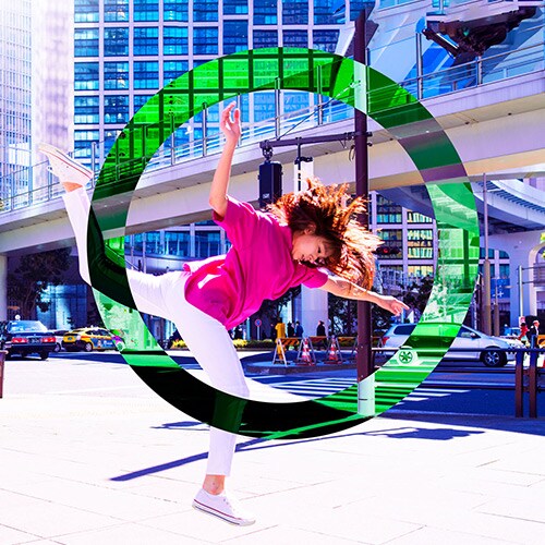 woman with brown hair on busy city street wearing pink shirt, white pants, and white sneakers jumping in the air with bright green circle around her